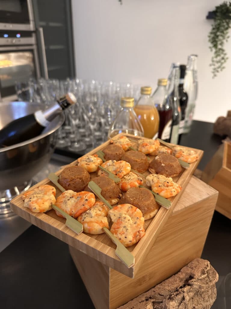 Plateau en bois d'amuse-bouches variés: brochettes de crevettes et petits fours salés, sur une table de buffet. Bouteille de champagne et jus en arrière-plan.