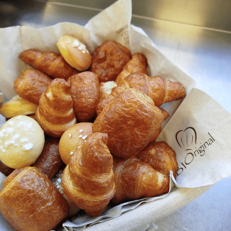 Assortiment de mini-viennoiseries dorées, dont des croissants et pains sucrés, dans un panier en tissu "BIO Original".