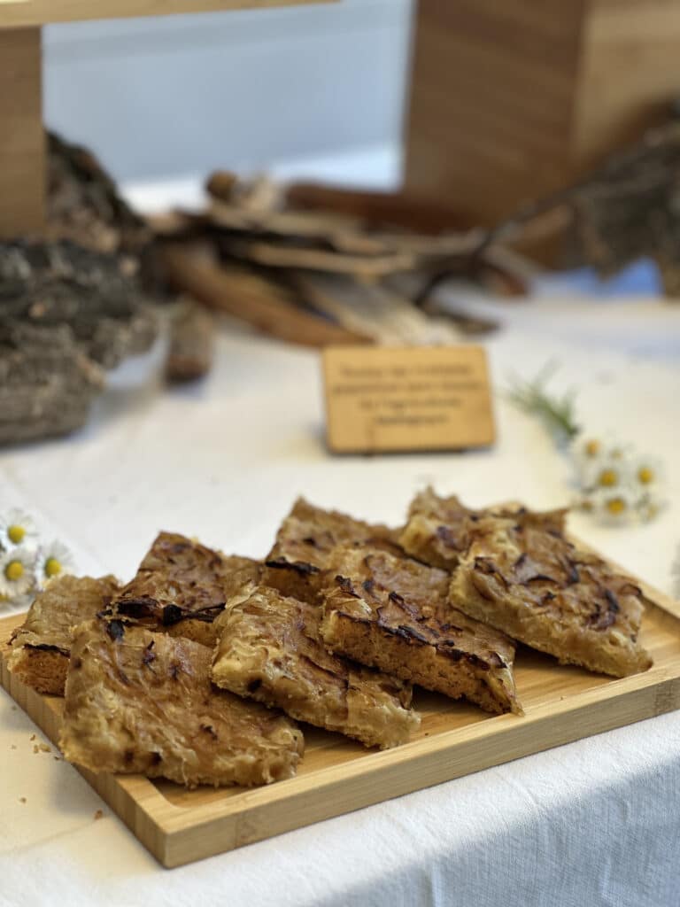 Tranches de tarte aux oignons caramélisés et feuilletée, posées sur un plateau en bois clair. Décor rustique flou en arrière-plan.