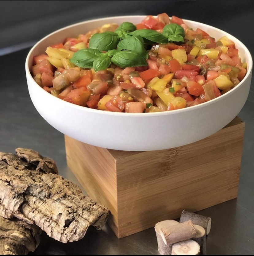 Bruschetta Tomates Basilic : Fraîcheur d'Été Bol blanc rempli de bruschetta fraîche de tomates rouges et jaunes, garni de feuilles de basilic, posé sur un bloc de bois.