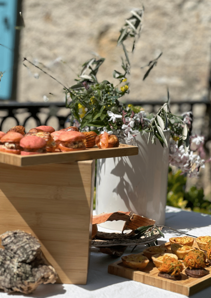 Buffet Apéritif Chic : Macarons Salés et Mini Quiches Buffet de bouchées apéritives, macarons salés et mini quiches sur supports en bois avec fleurs champêtres.