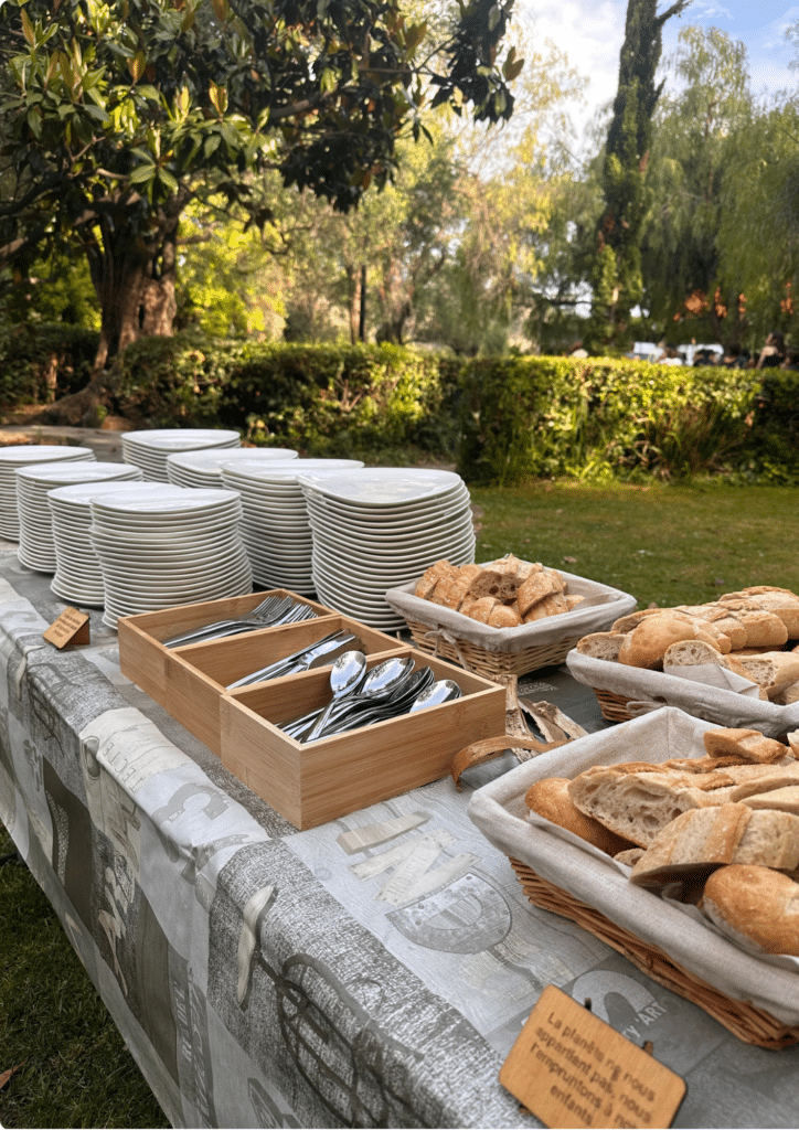 Buffet champêtre éco-responsable pour réception en plein air Buffet extérieur : piles d'assiettes, couverts, paniers de pain et panneau "La planète ne nous appartient pas".