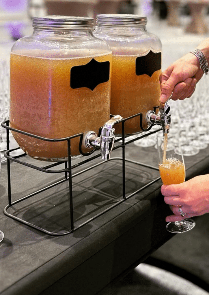 Distributeur de boisson en verre pour buffet et réception Distributeur de boissons en verre avec robinet versant un cocktail ambré dans une flûte lors d'un buffet.