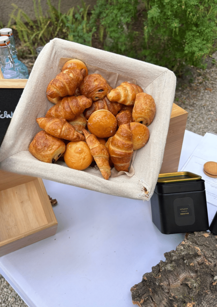 Mini viennoiseries et infusion menthe pour buffet Panier de mini viennoiseries et boîte d'Infusion Premium Menthe sur un buffet de petit-déjeuner en extérieur.